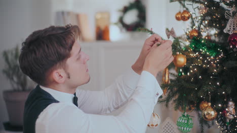 家でクリスマスツリーにバブルを吊るす服装の男