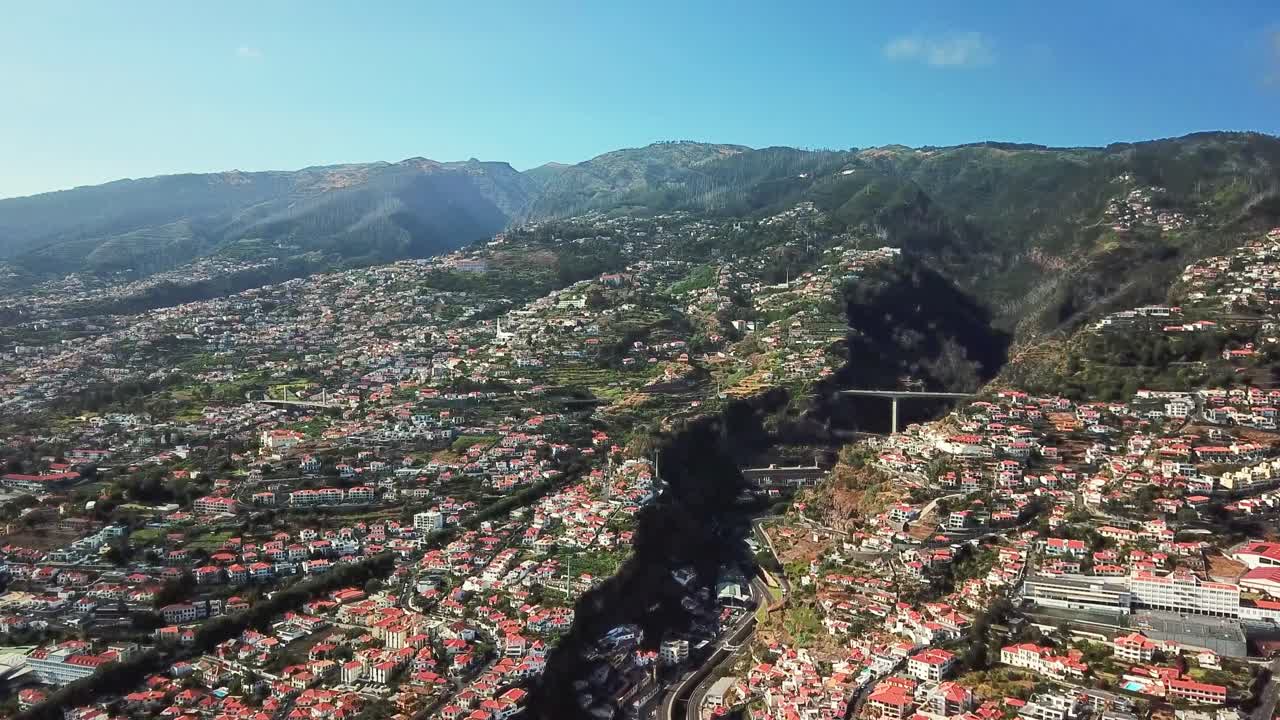 A stunning aerial view of Funchal Madeira, showcasing its vibrant cityscape, terracotta rooftops, and lush mountainous backdrop, highlighting its unique landscape and urban charm