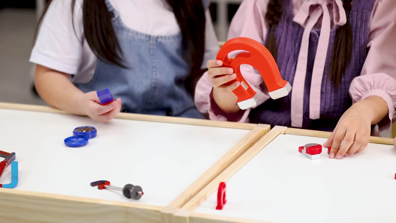 Close-up shot of children's hands using magnets for a physics experiment on a white table
