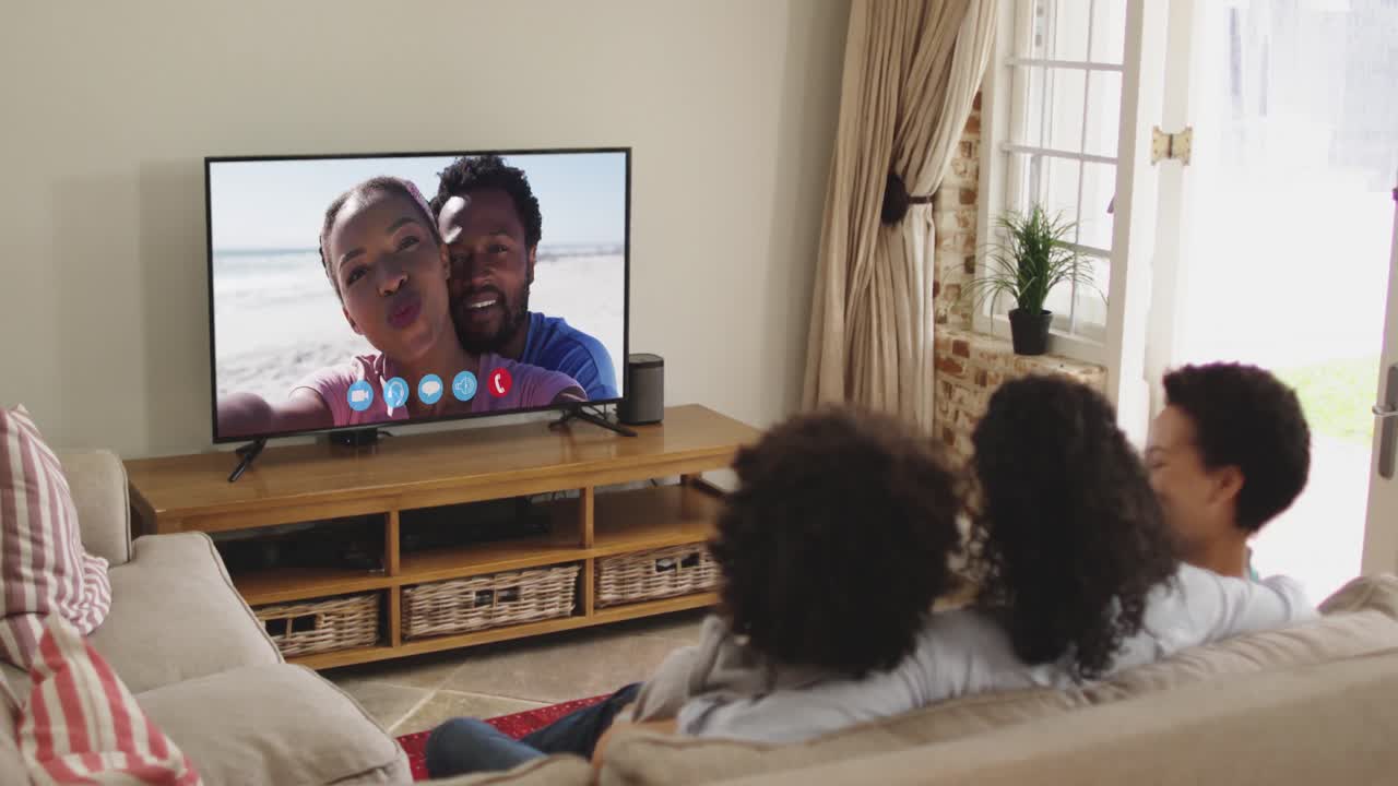 Famiglia afroamericana seduta sul divano che fa una videochiamata con amici sullo schermo della TV.