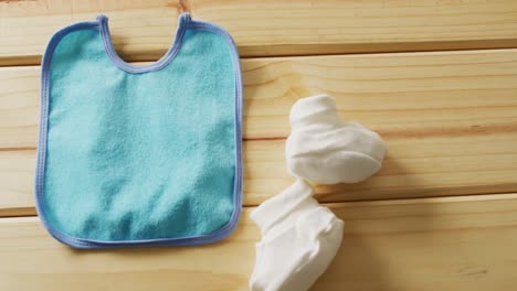 Video-of-close-up-of-blue-baby-bib-with-white-booties-on-wooden-background