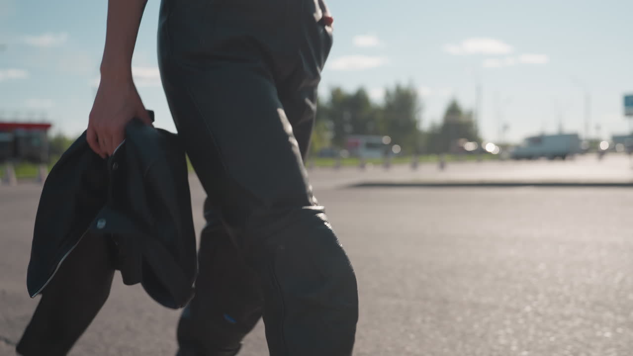 Close up of woman holding black leather jacket while walking in sunlight, showing strong sense of urban style, independence, and determination with blurred city background