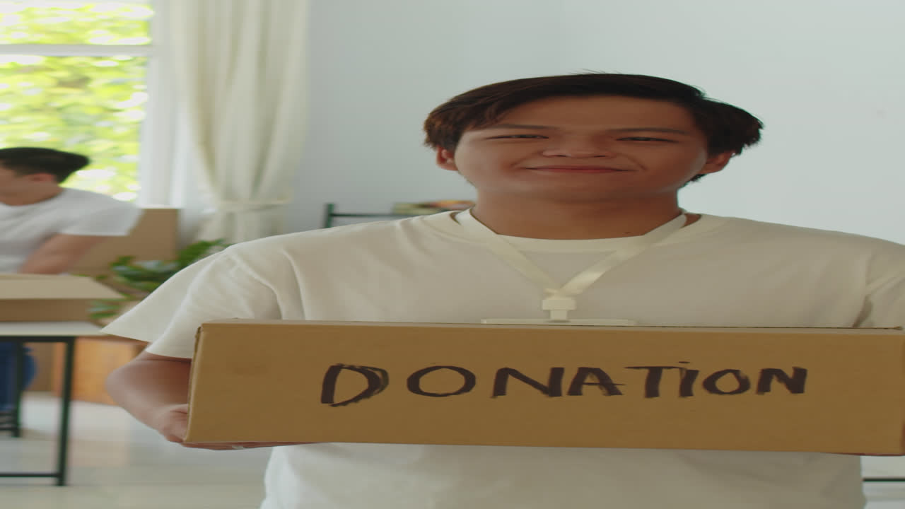 Asian Volunteer Holding Box with Collected Food and Clothes for Donation