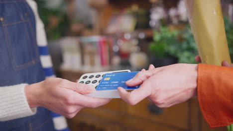 close up of female customer in florists shop making contactless payment for flowers with card