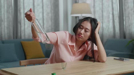 drunk, depressed asian woman with smartphone on table drinking vodka from the bottle at home