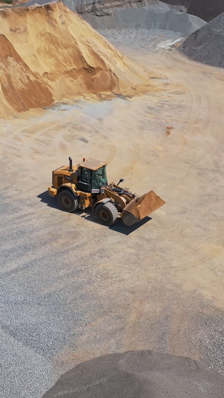 Aerial view of a modern industrial plant. Piles of rubble and sand on the huge territory of asphalt plant. Bulldozer transports sand. Vertical video