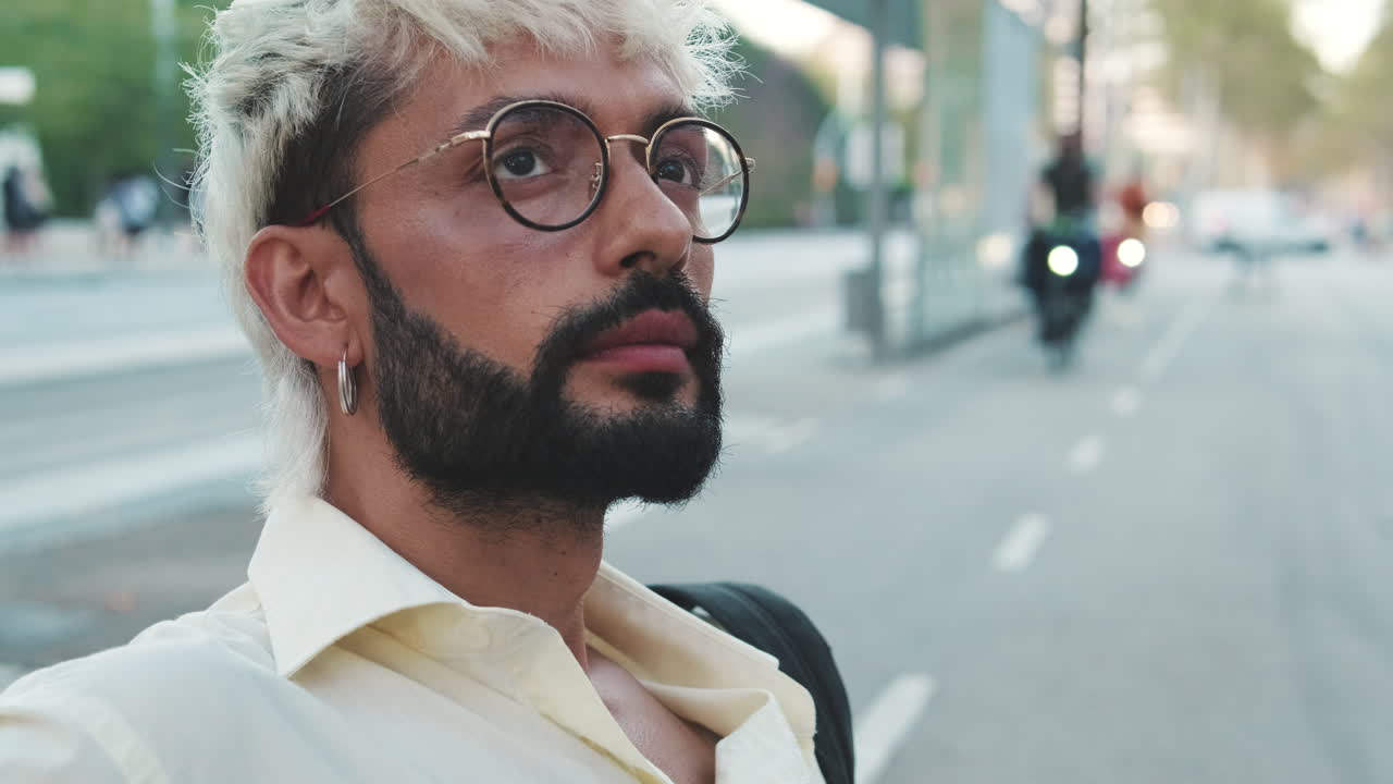 Giovane uomo con capelli decolorati e occhiali che guarda in alto in città.