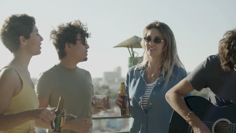 man playing guitar at rooftop party while his friends singing and dancing