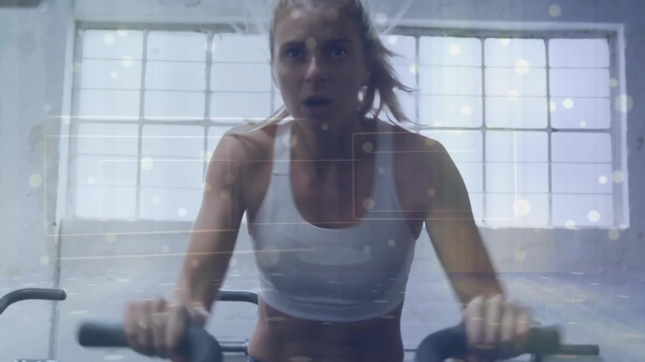 Woman starting pedaling bike in gym, leaning, overlay and wrist tracker tracking fitness intensity