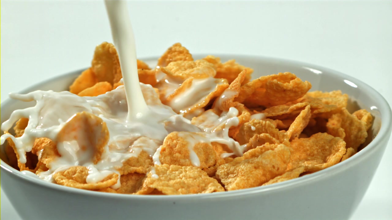 Slowmotion af mælk, der hældes ned i en skål med gyldne cornflakes