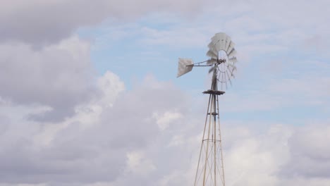 amplia toma de 4k de un antiguo molino de viento de granja rústico que sopla y gira en el viento con un cielo azul parcialmente nublado en el fondo
