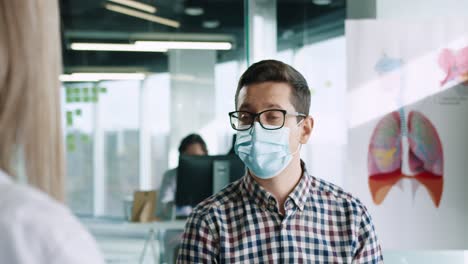 rear view of caucasian female doctor sitting at desk explaining treatment for coronavirus to male patient in medical mask in medical consultation