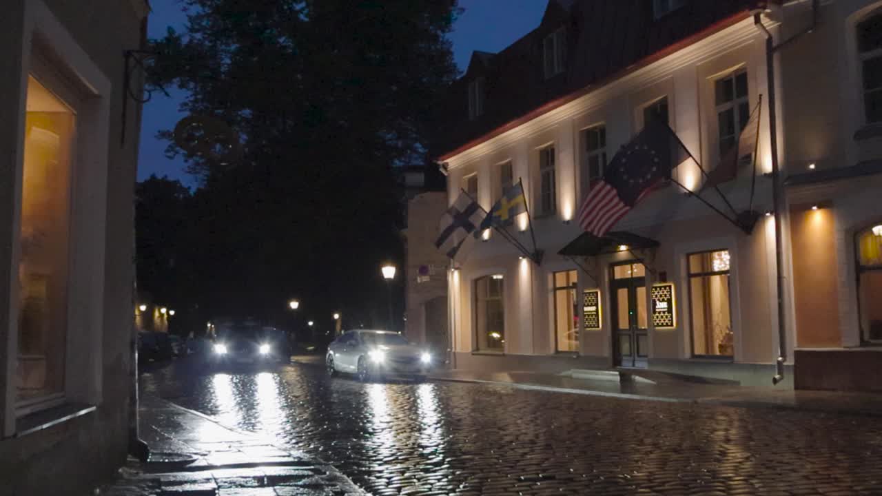 Historical old town also known as Hansa city during night time while cobblestones are wet and reflective beautifully. Cars are driving and reflecting their headlights on the ground. Old medieval house