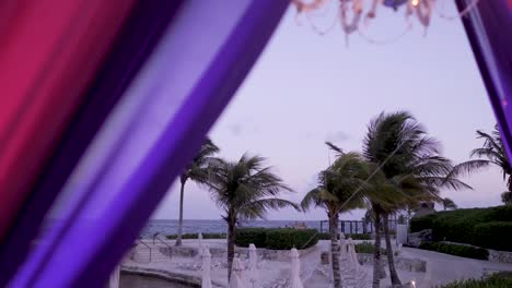 A-sliding-view-of-a-tropical-outdoor-dinner-setup-shot-between-purple-decorative-curtains