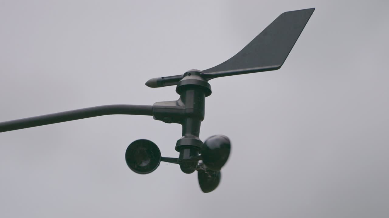 Close up, An Anemometer spinning and turning in the breeze with a grey and cloudy sky background.