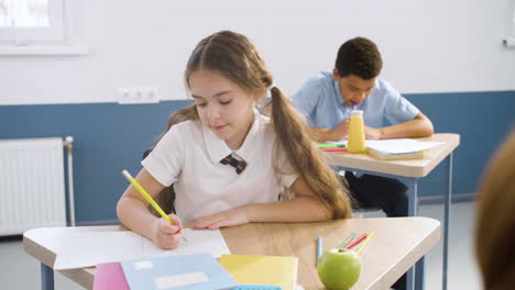 niña pequeña escribiendo en un cuaderno y luego pensando en algo durante la clase de inglés en la escuela