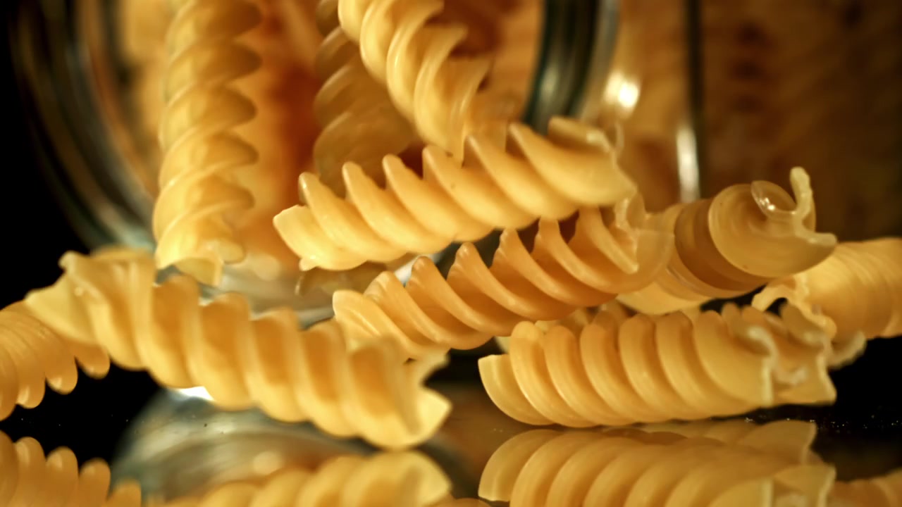 Pasta fusilli cruda che cade da un barattolo di vetro al rallentatore