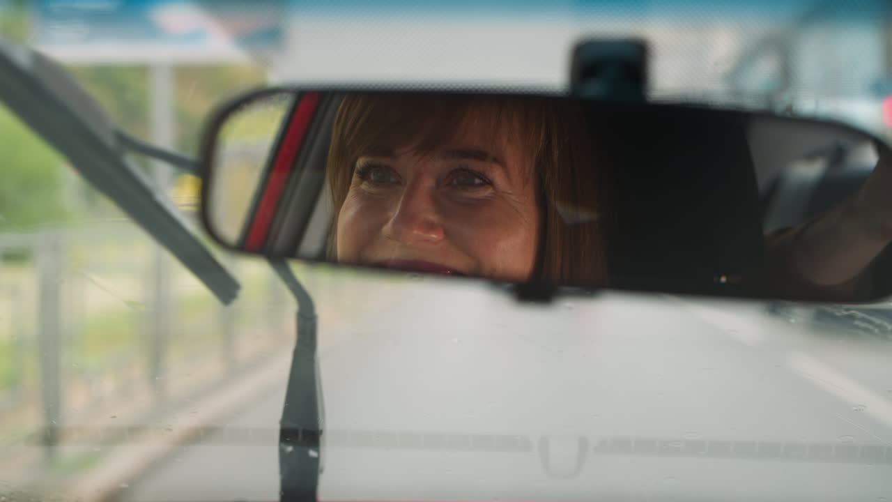 Donna allegra sorride guidando l'auto su strada deserta in una giornata piovosa.