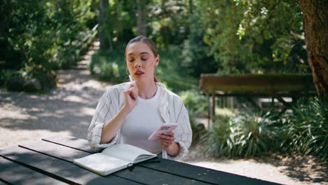 girl writer noting information to copybook from smartphone in forest close up.