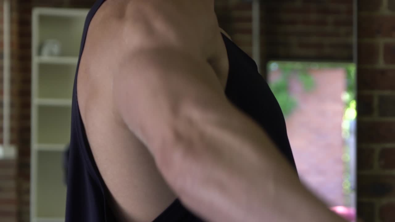 집 체육관에서 아령 레터럴 레이즈 운동을 하는 문신을 한 근육질의 남자