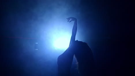 long-haired sportive woman moving gracefully. dancer performs in the dark room with projector at backdrop.