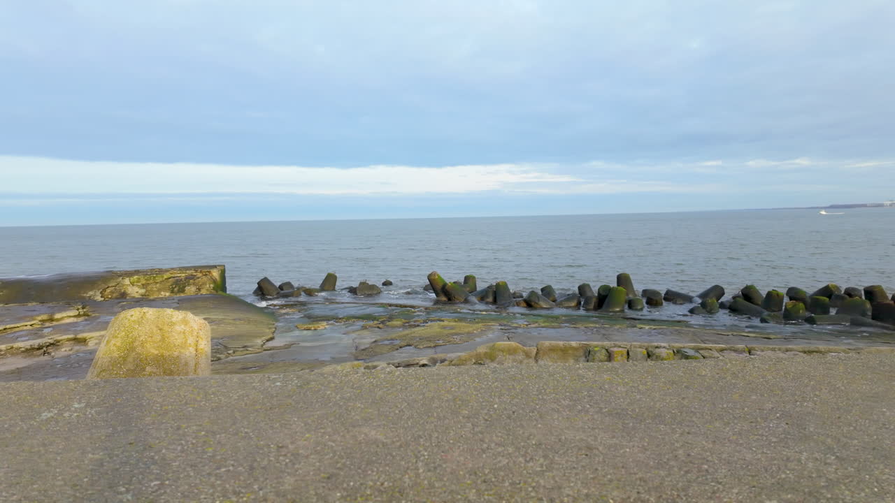 바다의 파도로부터 해안선을 보호하는 콘크리트 해안 파도, 배경에는 평온한 바다와 구름이 가득한 하늘