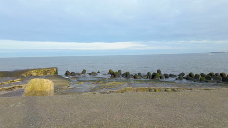 concrete coastal breakwaters protecting the shoreline from ocean waves, with a calm sea and cloudy sky in the background