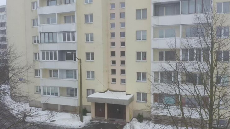 Ripresa ravvicinata con drone, inclinata verso l'alto, di un edificio giallo di nove piani in stile sovietico in una città innevata