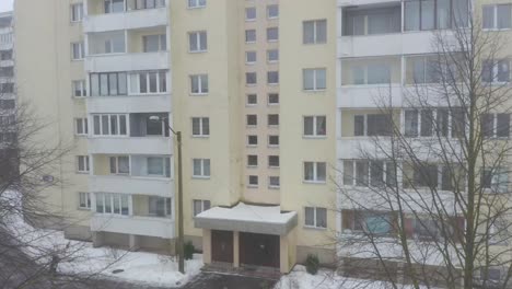 close drone tilt to up of a yellow nine-story soviet-style building in snowy city