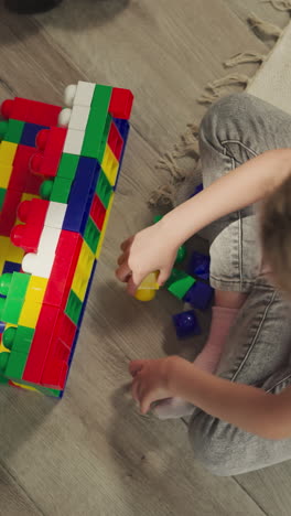 preschooler builds structure from plastic blocks sitting on floor. blonde girl with plait develops new skills with constructor upper close view