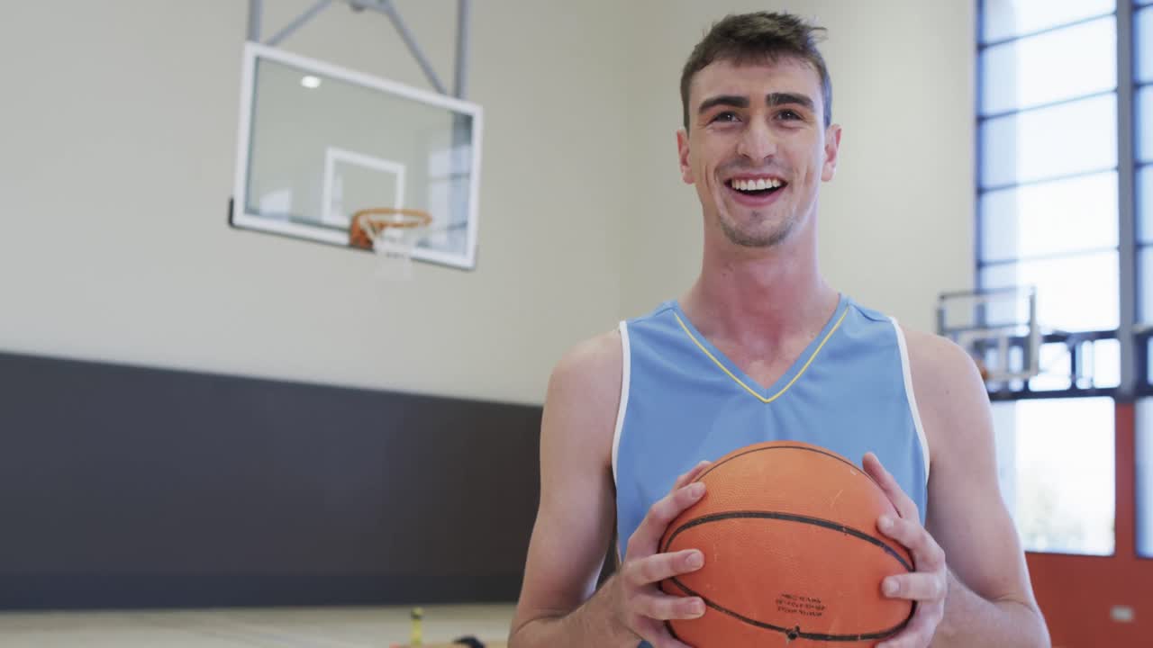 retrato de un jugador de baloncesto caucásico sosteniendo la pelota en una cancha cubierta, en cámara lenta