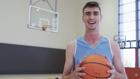 portrait of caucasian male basketball player holding ball in indoor court, in slow motion