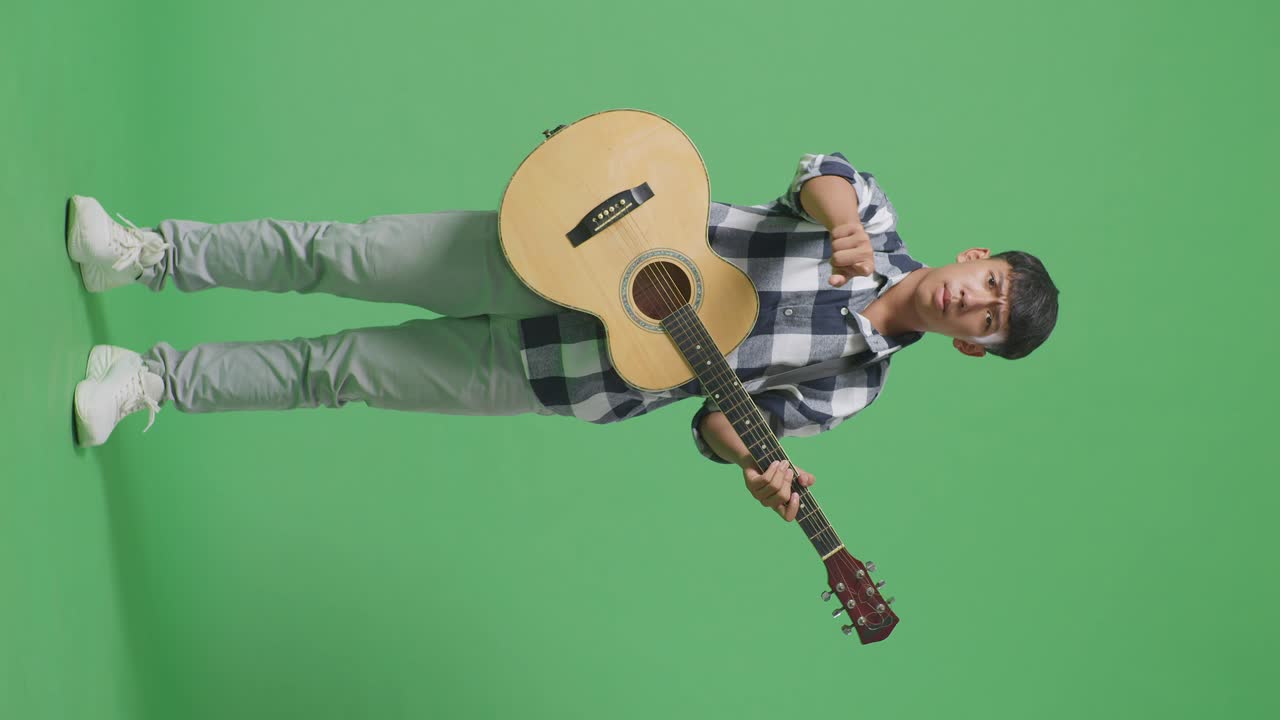 Figura intera di adolescente asiatico con chitarra che urla alla telecamera mentre è in piedi su sfondo green screen
