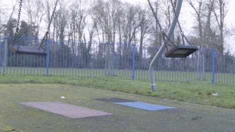 Empty-swinging-swing-on-children-playground-with-no-people-on-a-cloudy-cold-day-in-central-London