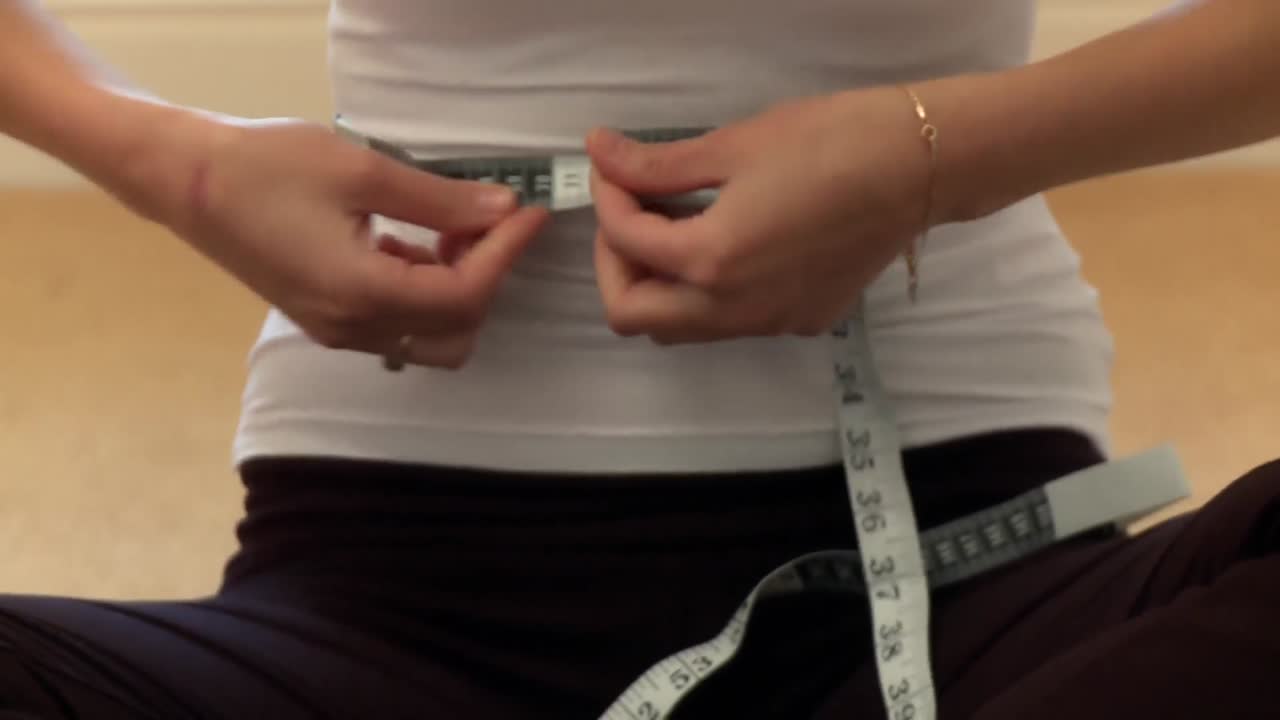 젊은 여성 이 허리 크기 를 측정 하고 있다