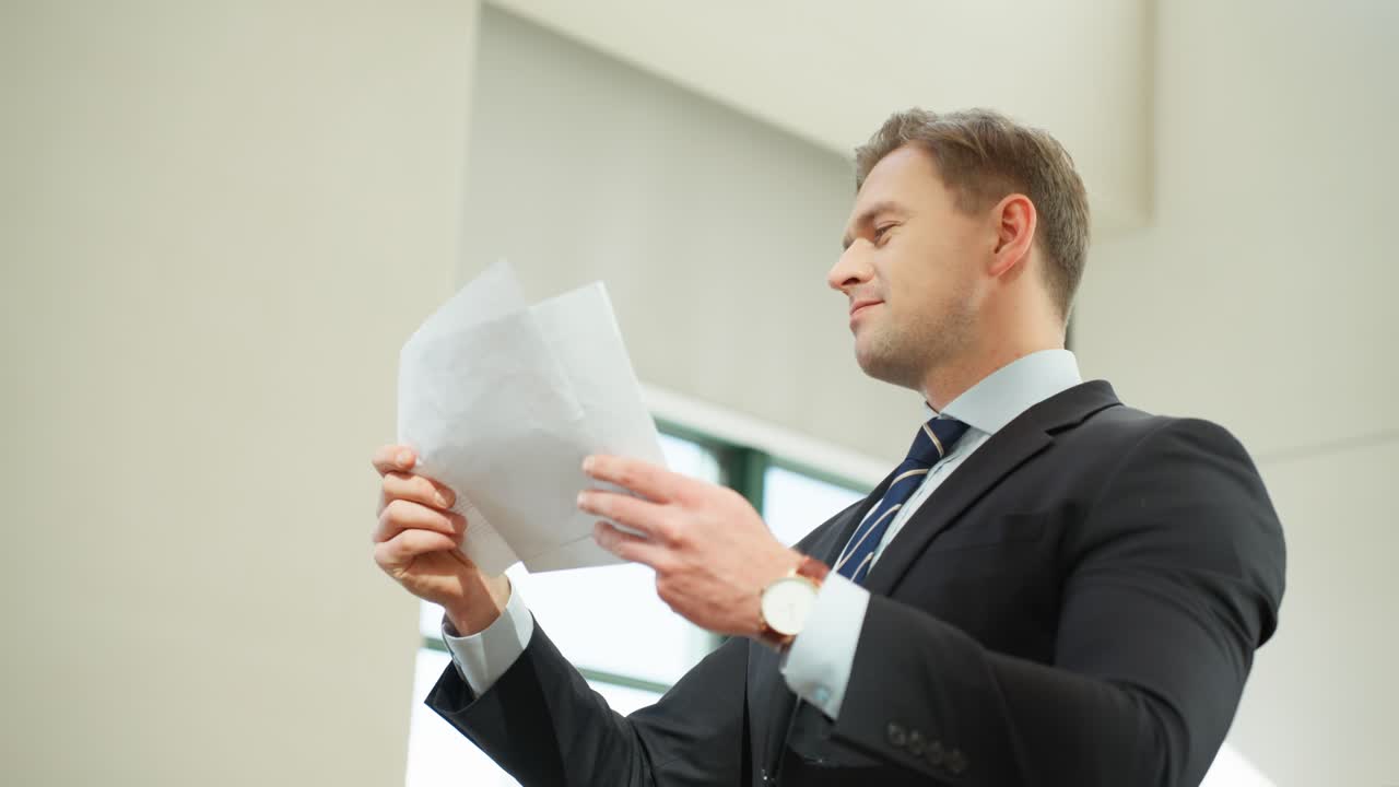 Low angle view of male CEO wearing formal suit reviewing business documents in office having satisfied facial expression - parallax shot