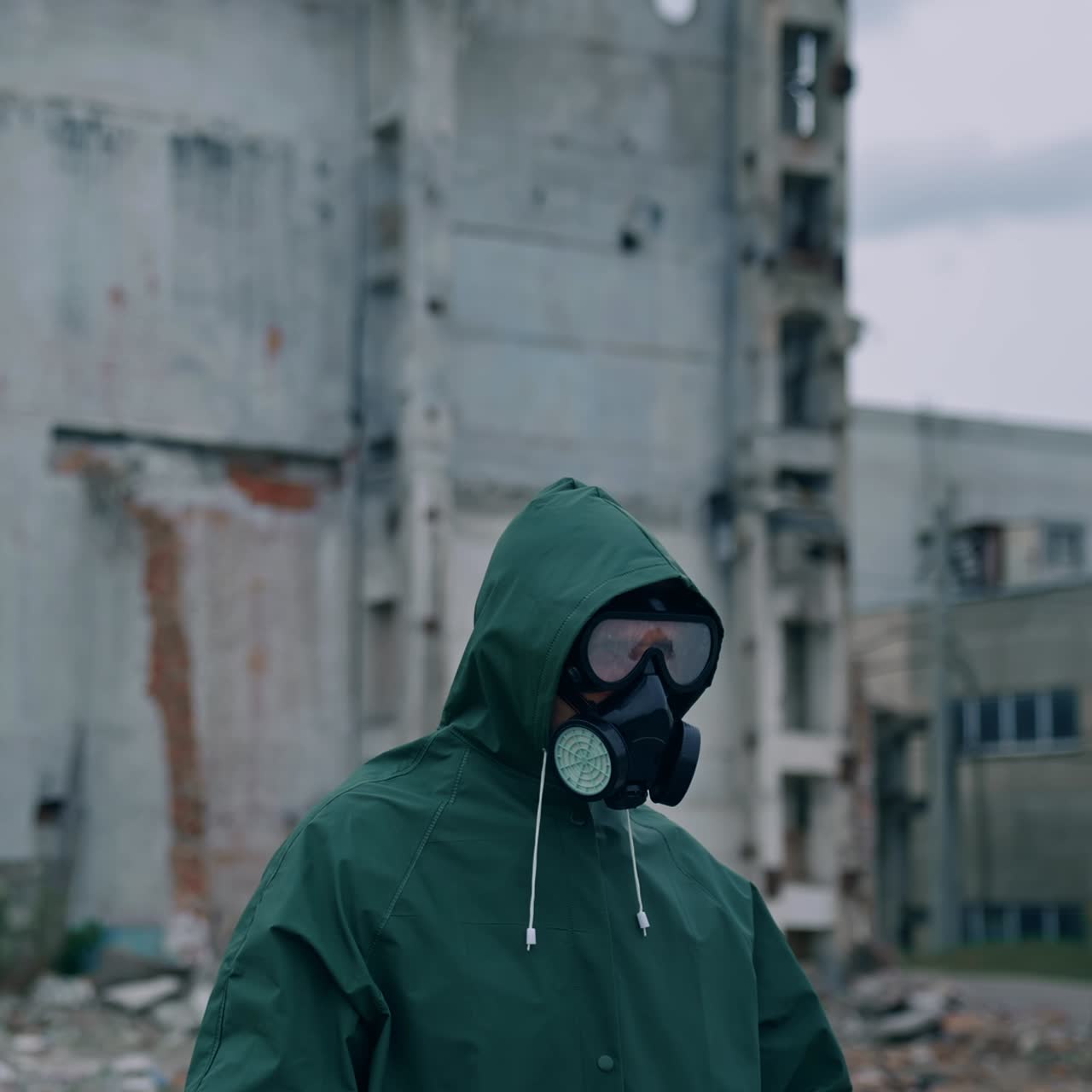 Human survivor standing alone in ruined place. Guy in the gas mask and safety clothes against the background of abandoned building. Apocalypse concept