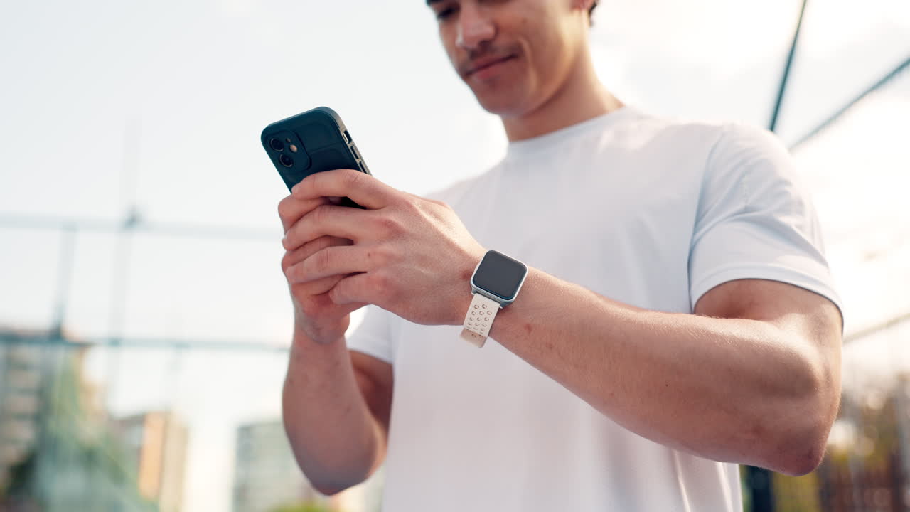 Young Man Smiling While Checking Smartphone and Smartwatch Outdoors