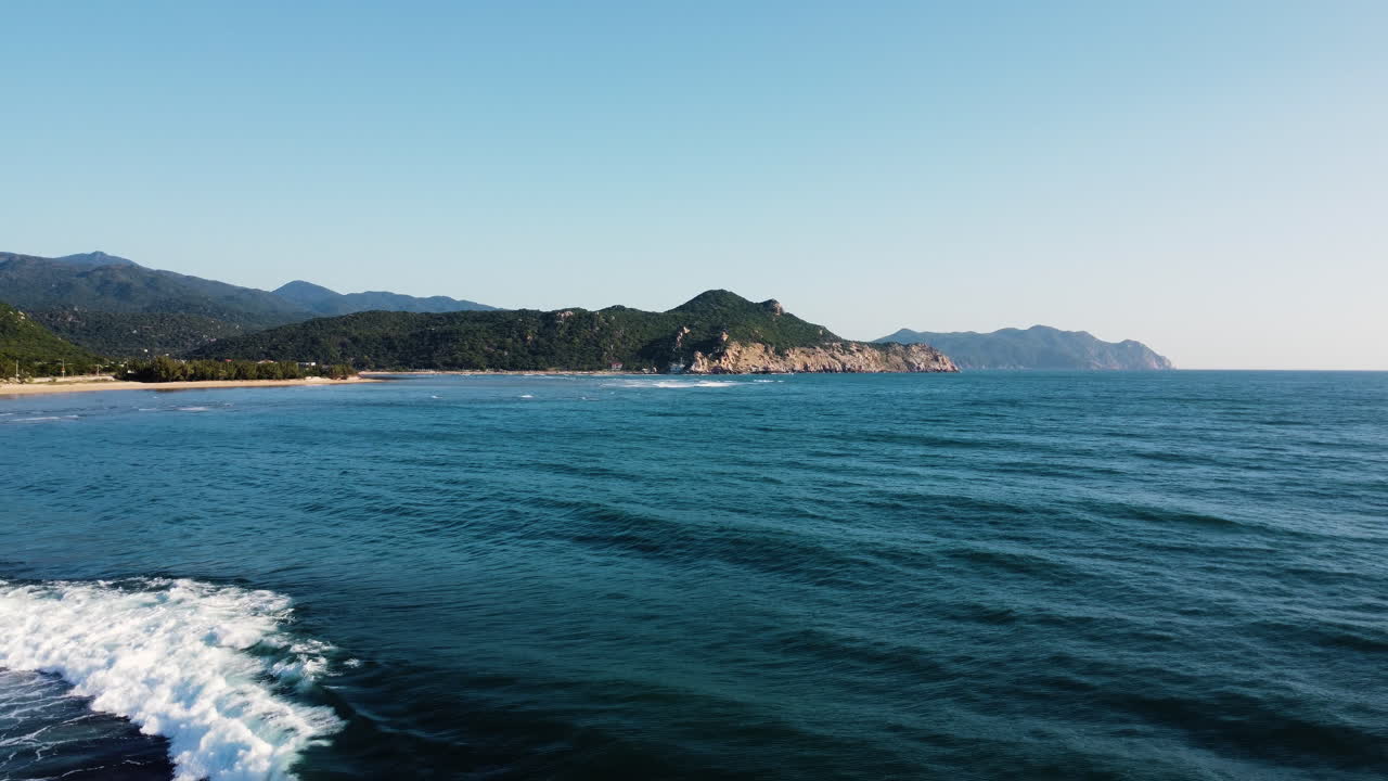 Volo di drone sopra l'acqua incontaminata dell'oceano nella Baia di Vinh Hy, maestoso paesaggio marino naturale di Hang Rai, costa con montagne e scogliere e cielo azzurro limpido.