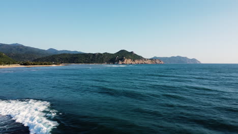 Drone-fly-above-pristine-ocean-water-in-Vinh-Hy-Bay,-Hang-Rai-majestic-natural-seascape-mountains-cliff-coastline-with-clear-blue-sky