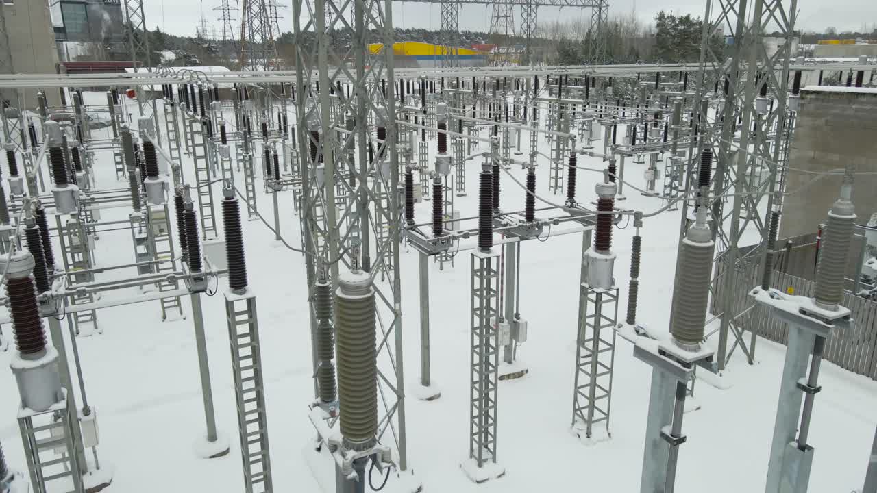 Low altitude aerial hover tilts upward across frozen substation insulators and cables, revealing snow covered grid structures and untouched white ground in a cold winter setting