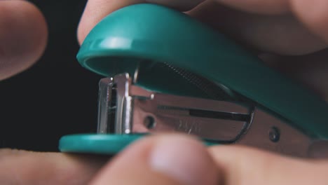 man-puts-clips-into-turquoise-stapler-on-dark-background