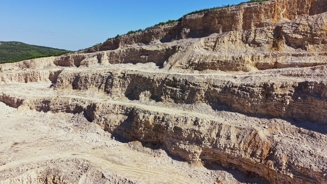 Una vista de una mina a cielo abierto con grandes capas de tierra expuestas y terreno rocoso durante el día en una zona montañosa
