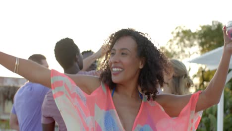 Happy-diverse-group-of-friends-dancing-holding-cocktails-at-beach