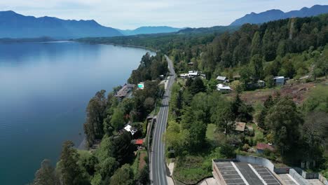 orbiting drone shot of a serene road skirting the edge of lake villarrica, surrounded by dense forest and distant mountains in southern chile