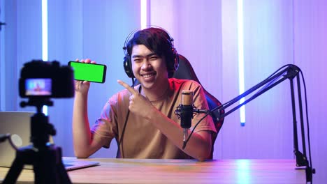 asian man holding mobile phone with mock up green screen while live stream with camera