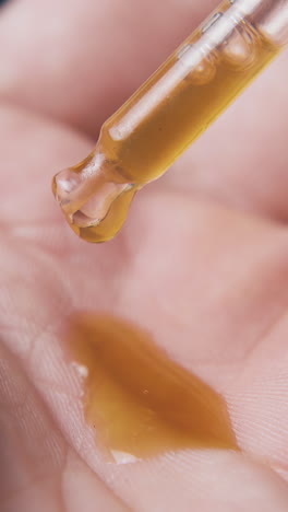 person drops brown liquid from glass pipette onto palm in black background extreme close view