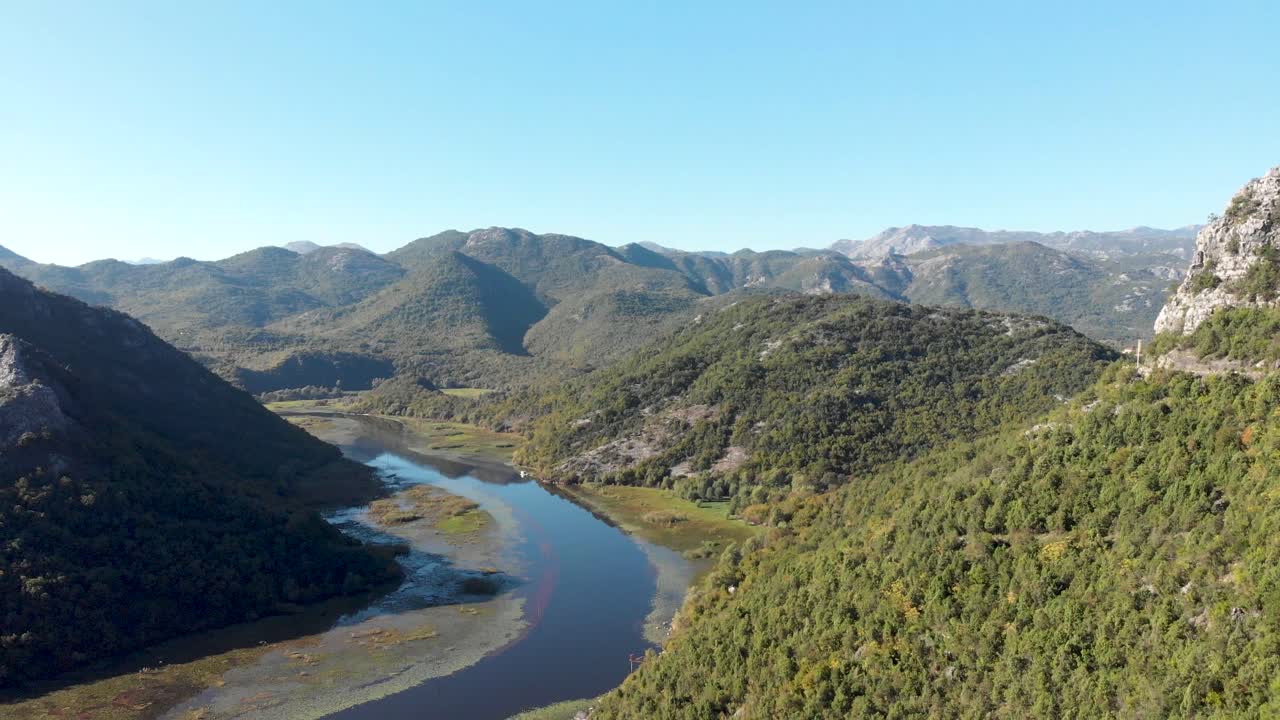 An aerial view of Lake Skadar in Montenegro on the bend of the river during a beautiful sunny day. Flying through trees to display the river below as the camera pans down