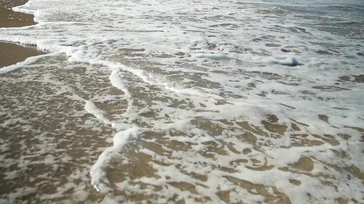 Dettaglio di onde con schiuma bianca su una spiaggia di sabbia dorata.