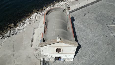 Aerial-drone-tilt-up-shot-flying-high-over-an-old-church-beside-Lake-Tekapo,-Pozzuoli,-Italy-on-a-bright-sunny-day